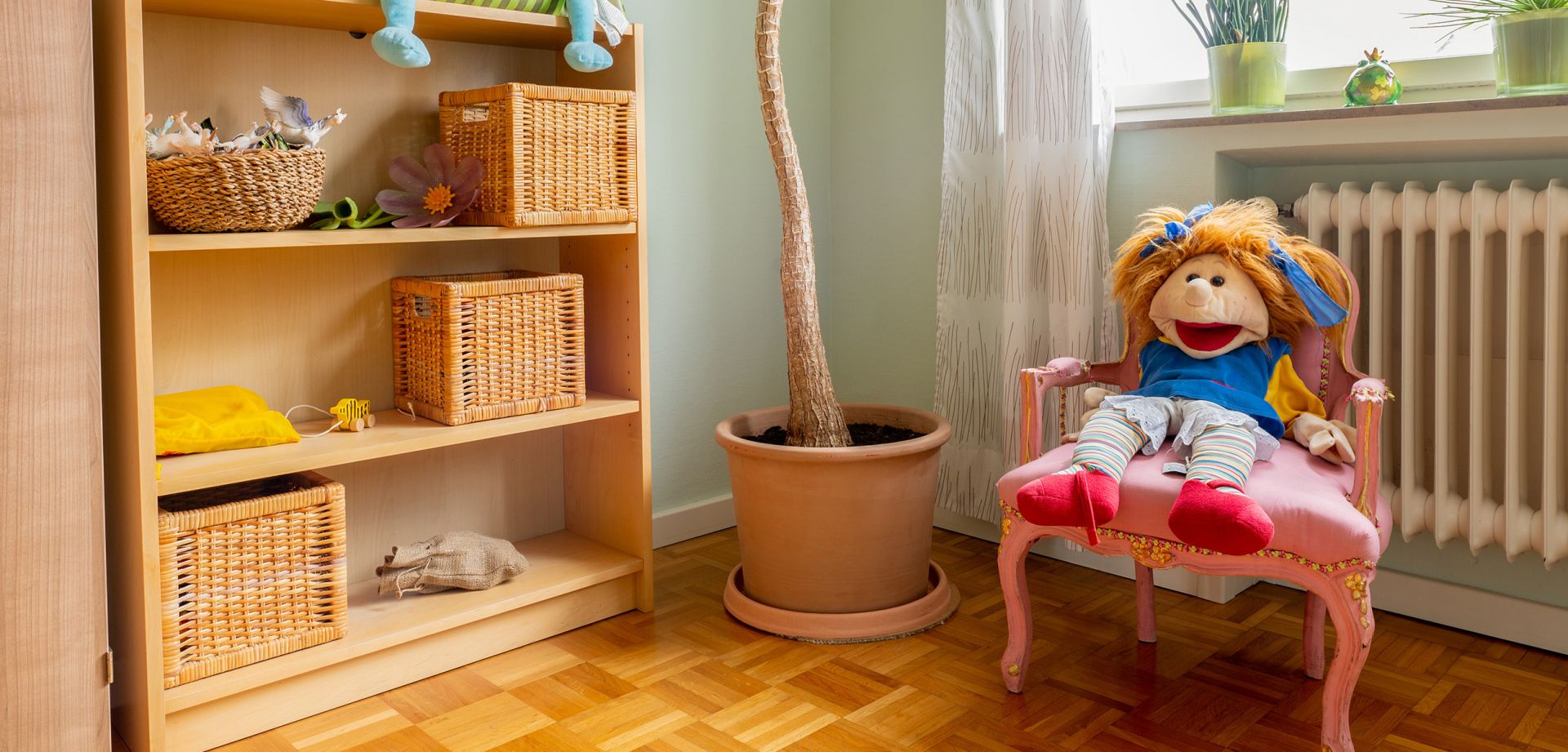Foto einer Stoffpuppe auf einem Stuhl sowie einem Regal mit verschiedenen Gegenständen und einem Pflanzentopf.